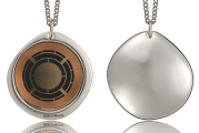 Two metallic pendant necklaces. One pendant features a circular design with a grid pattern, while the other has a smooth, plain surface. Both pendants are on silver chains.