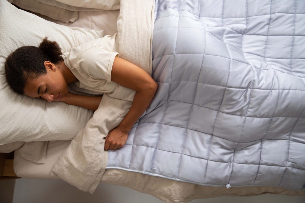 A woman practicing holistic health tips by making she she gets quality sleep time in a comfortable bed with a blanket.