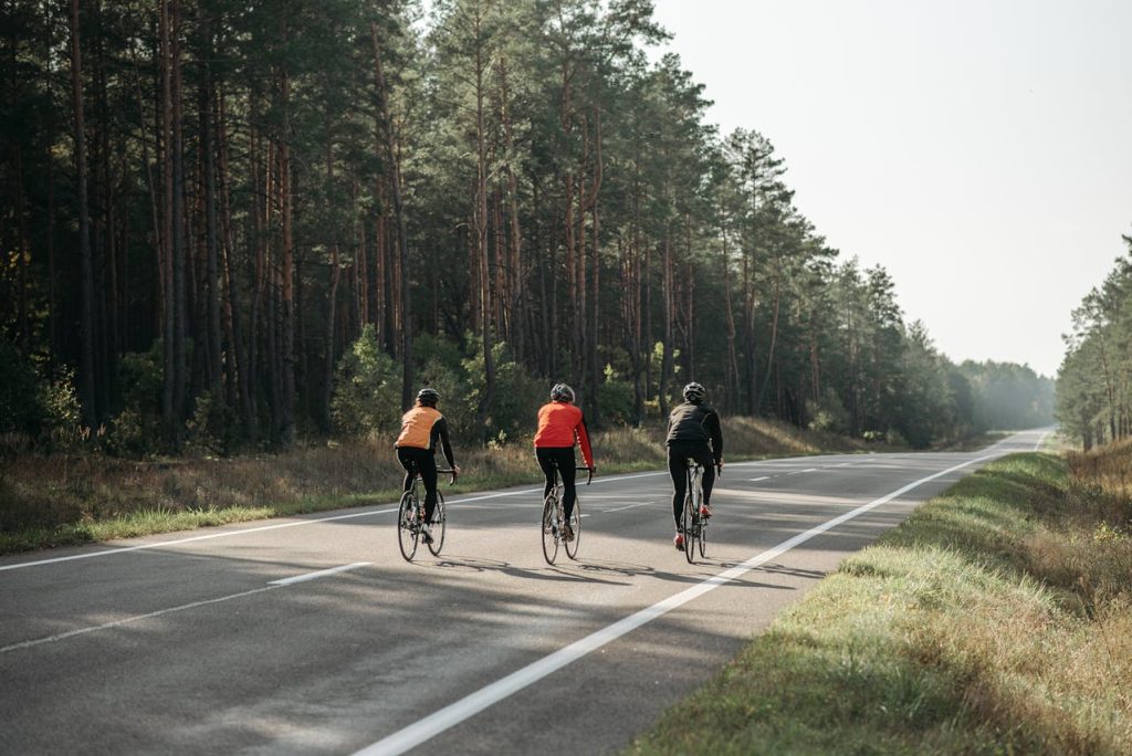 Three female cyclists ride on a forest-lined road with clear skies above, their energy levels soaring as if propelled by the natural boost of hormone leptin.
